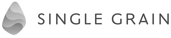 A logo featuring a stylized, gradient grey teardrop-shaped symbol on the left, followed by the words "SINGLE GRAIN" in uppercase, modern, grey lettering.